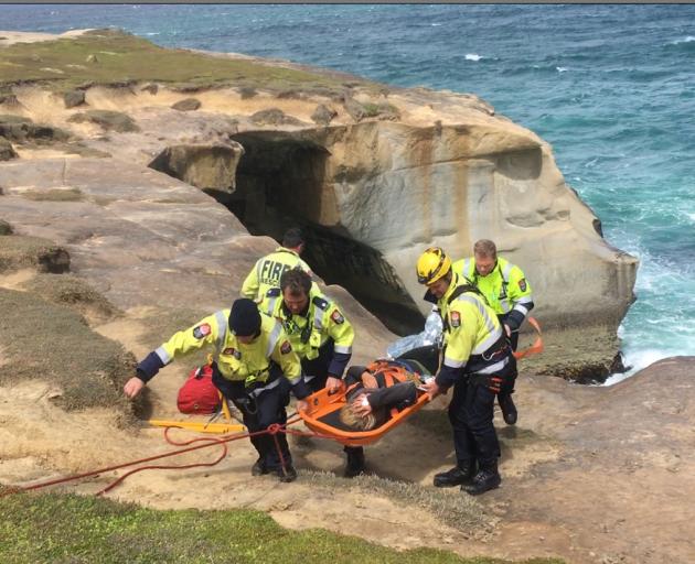Rescuers carry a 25-year-old woman in a stokes basket after she slipped and fell  at Tunnel Beach...