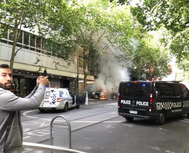 A pedestrian takes a photo of the car in flames. Photo: Twitter