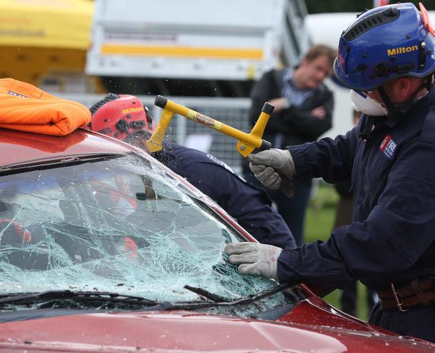 Members of the Milton crash rescue team break the windshield of a wrecked car as they...
