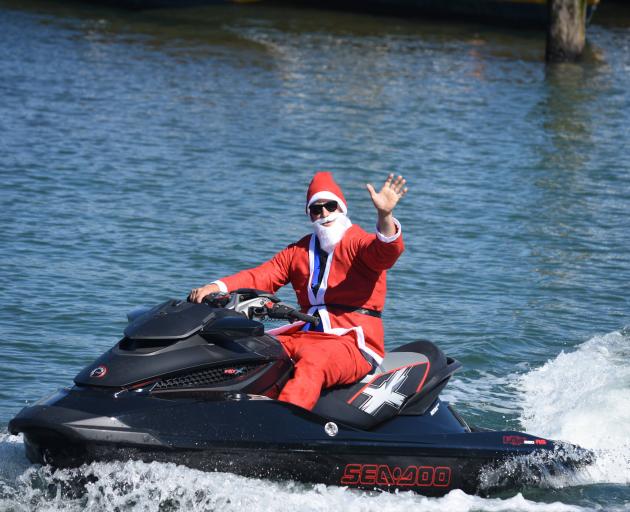 Jayden Henderson waves at tourists and bystanders while riding his jet ski dressed as Santa Claus this morning. Photo: Lisa Henderson