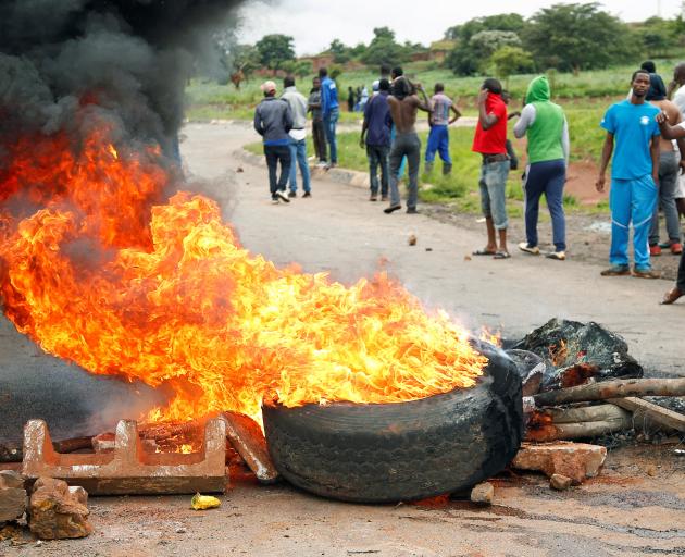 Protesters stand behind a burning barricade on a road leading to Harare. Photo: Reuters 