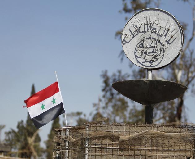 A Syrian national flag flutters next to the Islamic State's slogan at a roundabout where...