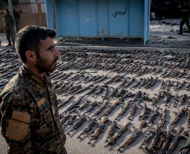 A Syrian Defence Forces soldier looks over seized ISIS weapons in the Syrian town of Beghouz....