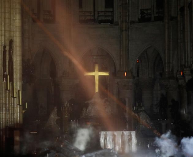 Smoke rises around the alter in front of the cross inside the Notre Dame Cathedral as a fire...