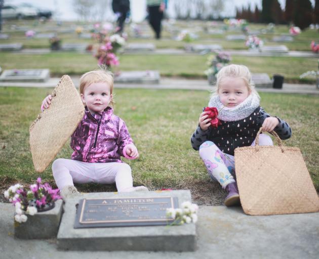 Peyton McAuley (left, 1) and Chloe Angland (3), from Barnardos Home-based early learning, place posies at the grave of A. Familton, who is buried in the services section of the Oamaru Cemetery, as part of an annual children's posy-laying ceremony yesterda