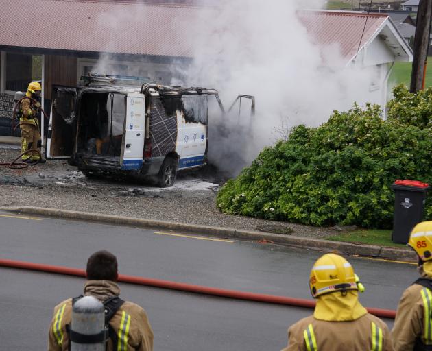 Smoke clouds the front of the van as fire crews attempt to extinguish the fire. Photo: Sean Nugent