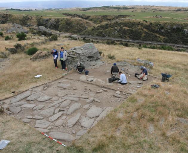 University of Otago archaeology students excavate the schist slab foundation of a large building,...