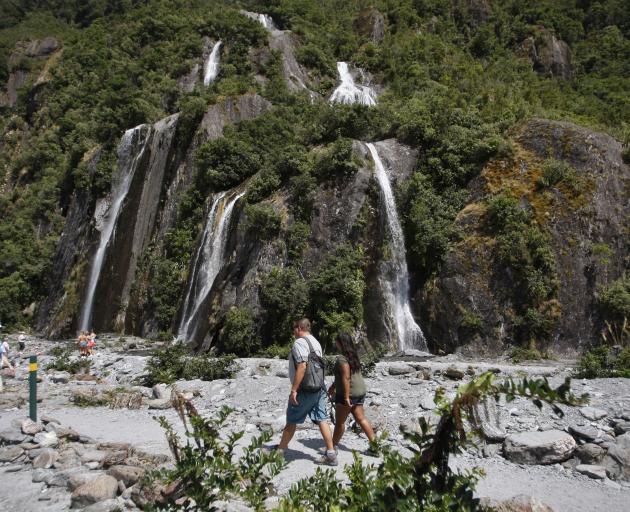 Tourists walk past waterfalls at the Franz Josef Glacier in summer. Photo: AP
