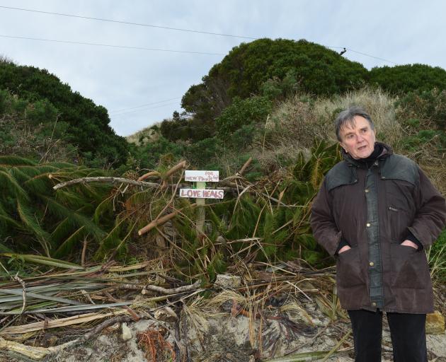 Aramoana Conservation Charitable Trust member Adrian Hall stands in front of piles of vegetation...