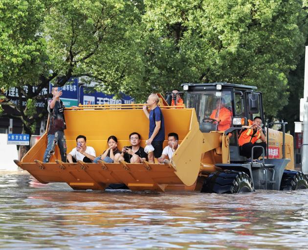 Rescue workers evacuate stranded residents with a bulldozer on a flooded street after typhoon...