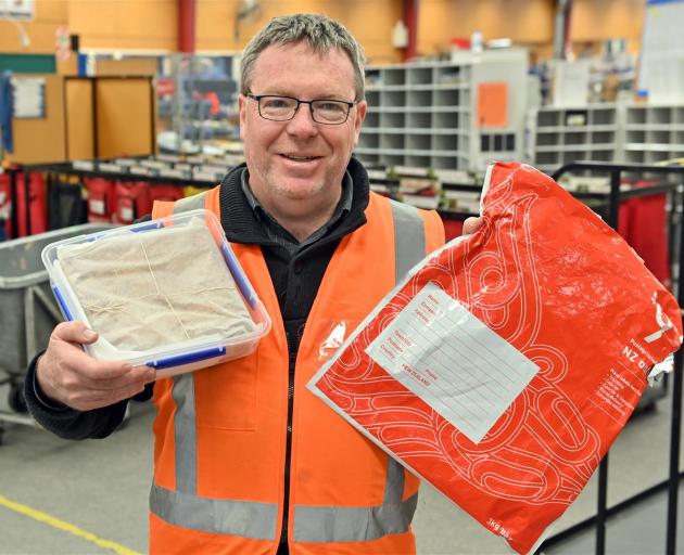 New Zealand Post Coastal Otago area manager Craig Strathern holds a mysterious homemade fruitcake...