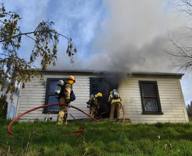 Firefighters get a hose into a burning home in Woodhaugh yesterday, after smashing the glass...