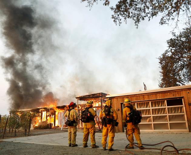 Firefighters look on as a house burns in the wildfires north of San Francisco Bay, California....