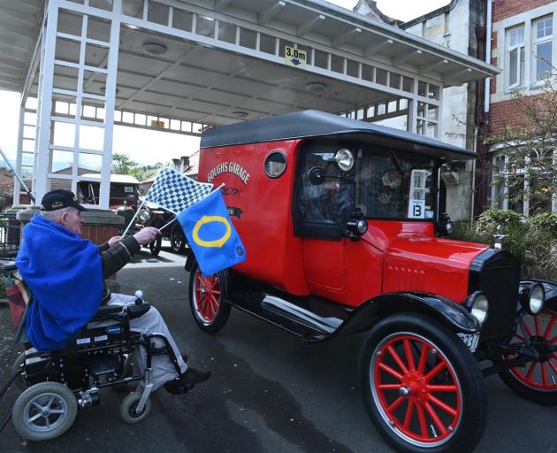 Ross Home resident Trevor Rodger (80) waves away vintage vehicles with his starting flags...