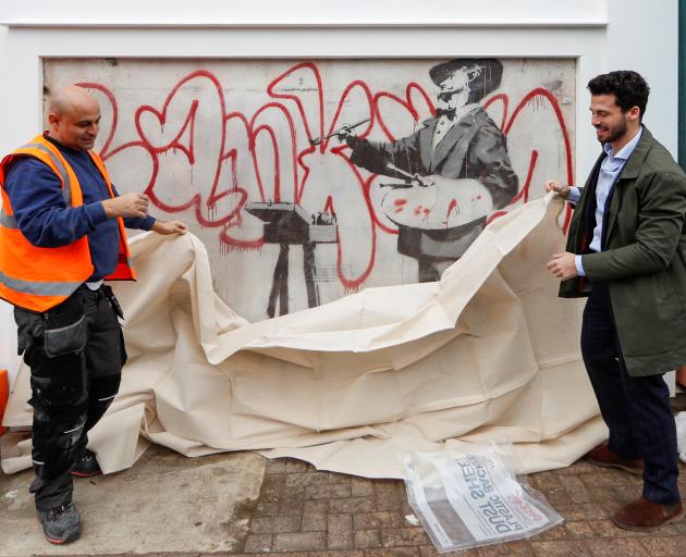 Men place a sheet over a Banksy mural known as The Painter, which first appeared in 2008, before it is officially unveiled in Notting Hill, London. Photo: Reuters