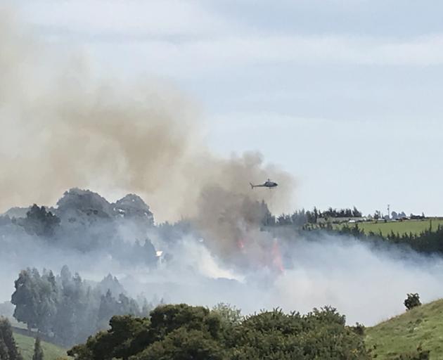 A helicopter with a monsoon bucket fights the fire on Scroggs Hill as seen from Kayforce St, Ocean View. Photo: Jacqueline Parsons