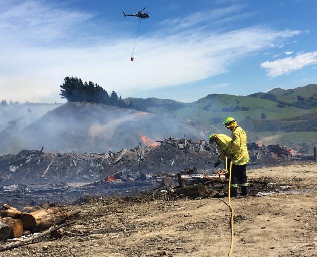 Firefighters battle the blaze at Bucklands Crossing while a helicopter with a monsoon bucket fights the blaze overhead. Photo: Stephen Jaquiery