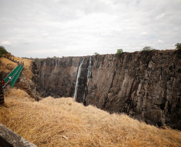 Visitors walk over a bridge as dry cliffs are seen along the parched gorge on the Zambian side of...