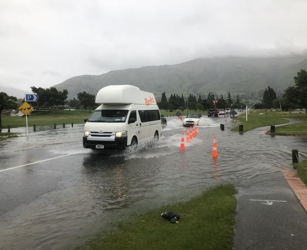 Cars drive through a flooded part of Ardmore St in Wanaka this morning. Photo: Kerrie Waterworth