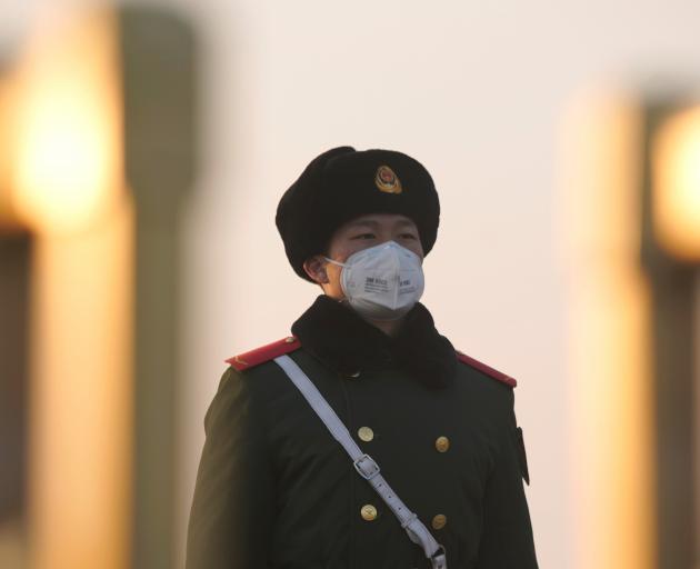 A paramilitary officer wearing a mask stands guard at the Tiananmen Square, as the country is hit...