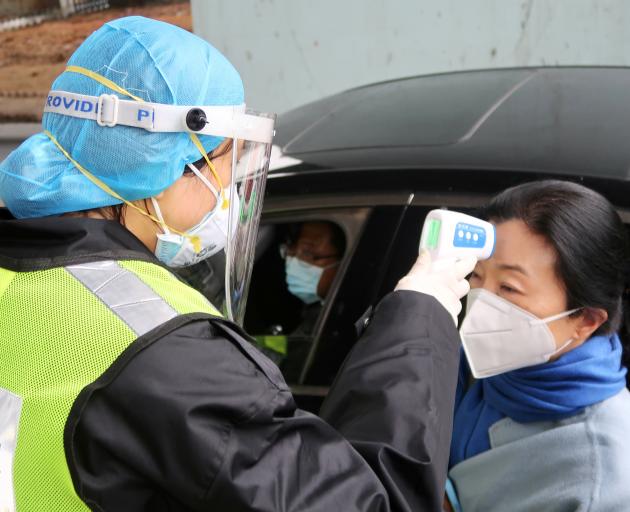 A security officer in a protective mask checks the temperature of a passenger following the...