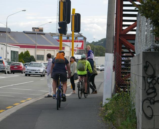 Pedestrians wait at the crossing in Thomas Burns St as cyclists head south on the footpath by the overbridge. PHOTO: JESSICA WILSON