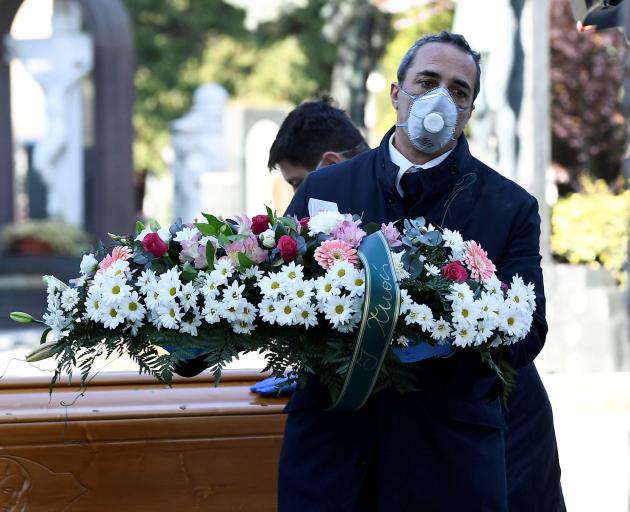 Cemetery workers and funeral agency workers in protective masks transport a coffin of a person...