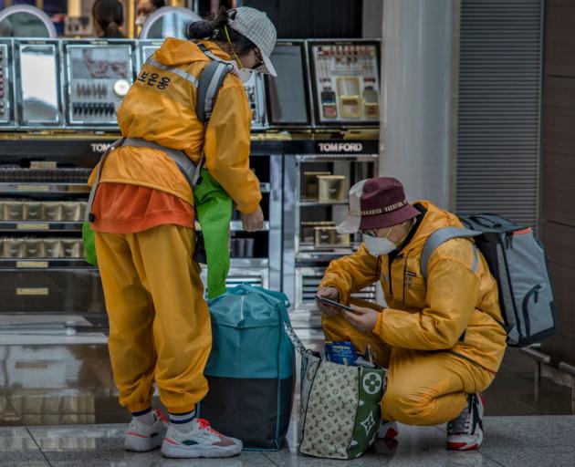 Travellers wear rain suits and face masks to protect themselves from Covid-19 while waiting for...