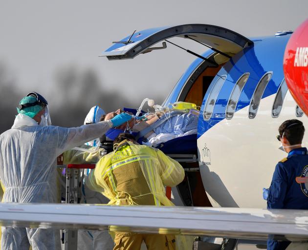 A coronavirus infected patient from France is transferred from an ambulance aircraft to an...