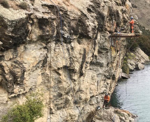 Workers pay attention to an area of cliff face in the Reilly Bluff during construction of the...