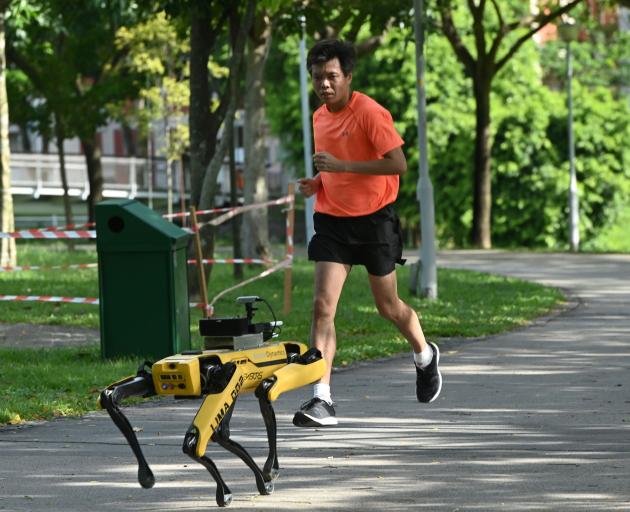A man jogs past a four-legged robot called Spot, which broadcasts a recorded message reminding...