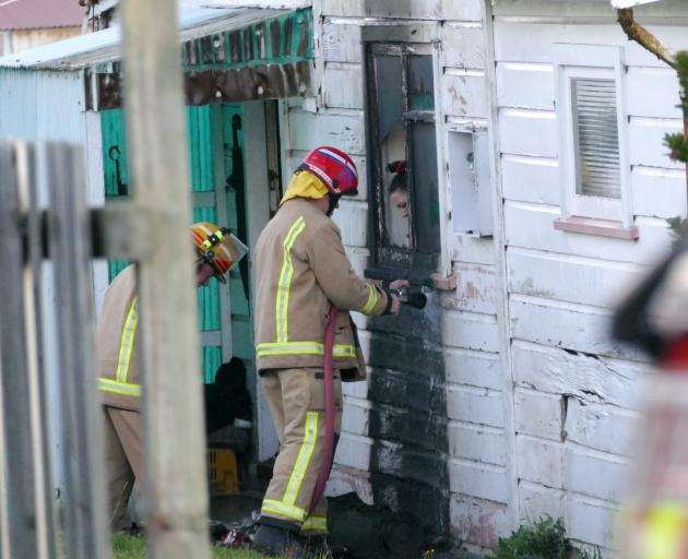 A Kaitangata homeowner looks on as firefighters damp down hotspots at the side of her Christchurch St house today. Photo: Richard Davison