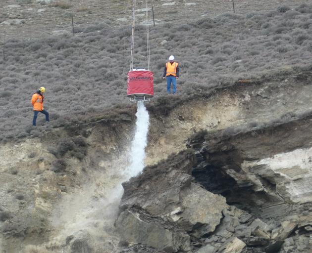 Engineers direct a helicopter monsoon bucket to wash out loosened rock debris from a slip above...