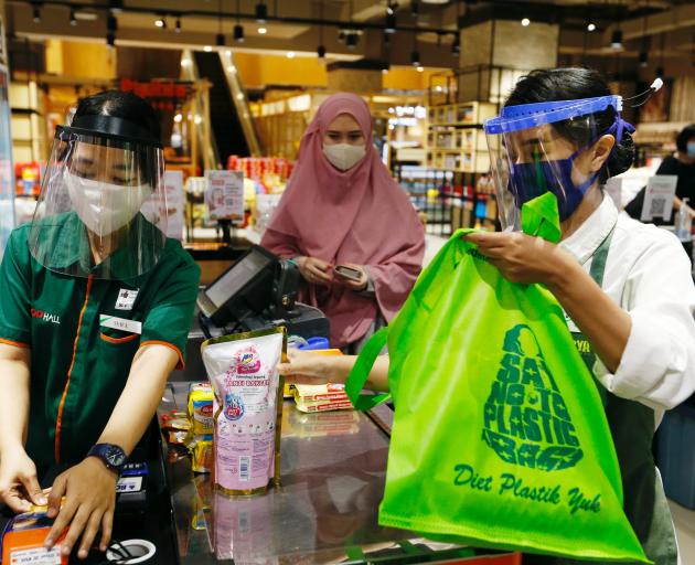 A worker wearing a face shield and protective mask use a tote bag to replace plastic at a...