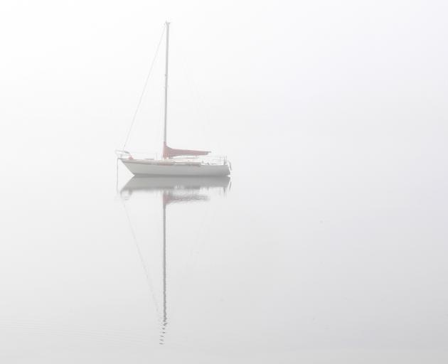 A yacht sits anchored in the fog off Grassy Point by Portobello Rd yesterday. Photo: Stephen...