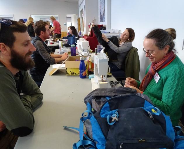 Dave Stewart, of Hawea Flat, watches Ros Goulding, from Deep Canyon, sew a tear in his backpack...