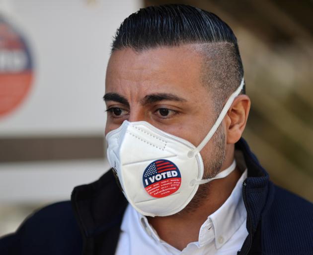 A man wears an “I Voted” sticker on his mask after voting in the US presidential election in Los...