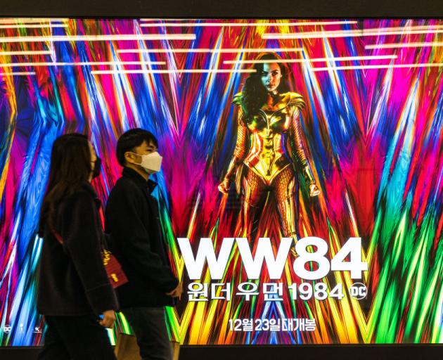 People wearing masks walk past an advertising billboard of the movie 'Wonder Woman 1984'. Photo:...