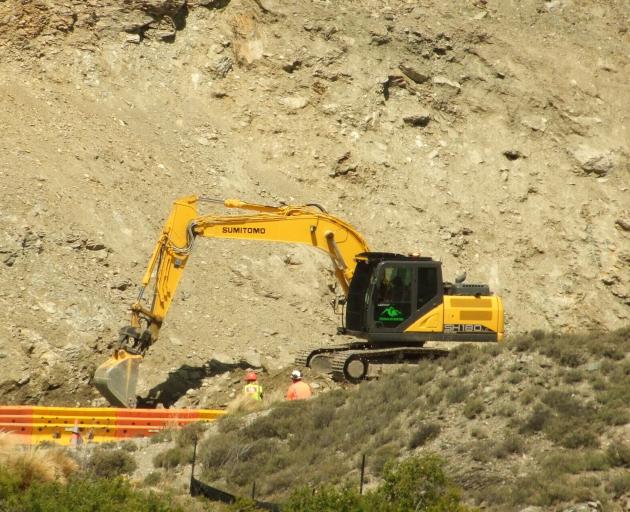 An excavator works to clear debris from the base of the slip that loomed over State Highway 8 in...