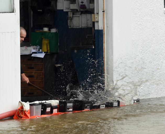 A Normans Auto Electrical employee sweeps water out of the building during yesterday’s flooding...