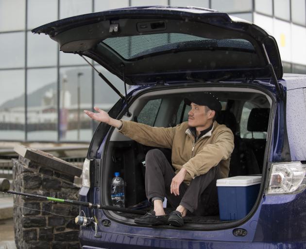 Yi Bai, of Dunedin, shelters from the rain in the back of his station wagon as he fishes for...