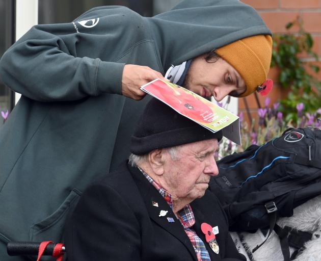 Liam Penman uses his service sheet to protect his grandfather Allan Penman (86) from the rain at...