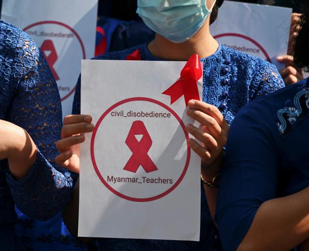 A teacher from Yangon University of Education holds a sign with a red ribbon while taking part in...