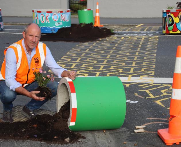 Gore District Council roading asset manager Peter Standring squats next to a vandalised planter...