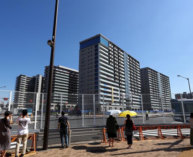 People stand next to fences as they take pictures of the athletes village in Tokyo. Photo: Reuters 