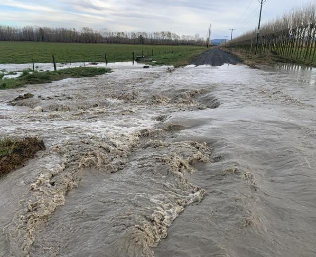 Water surges down Springfield Road via a breach of the north branch of the Ashburton River at the...
