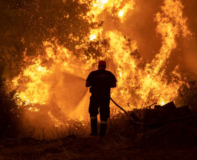 A firefighter tries to extinguish a wildfire burning in the village of Pefki, on the Greek island...