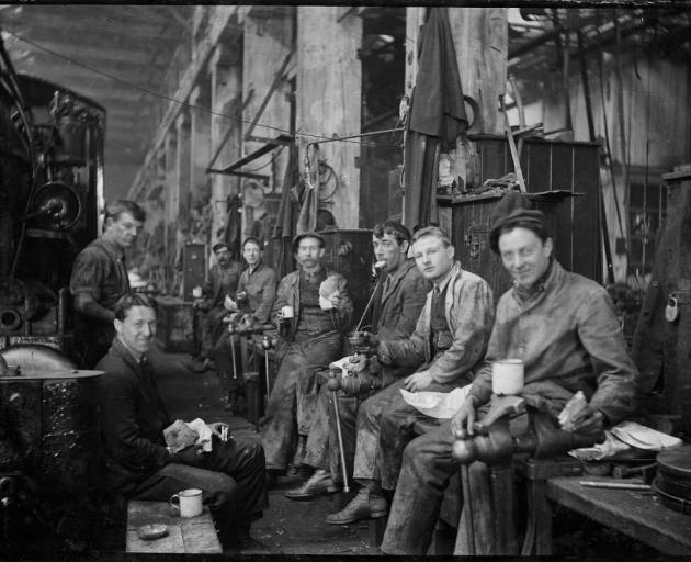 A group of men takes their lunch break, seated in one of the Hillside Railway Workshops, circa...