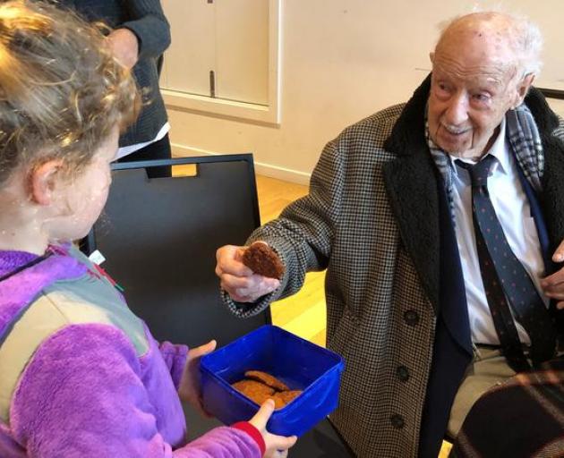 Madison Webb baked Anzac biscuits for veterans at the RSA in Christchurch. After the dawn service she gives one to 106-year-old veteran, sergeant Bill Mitchell, who fought in the Pacific during his time in the defence force. Photo: RNZ / Brooke Jenner