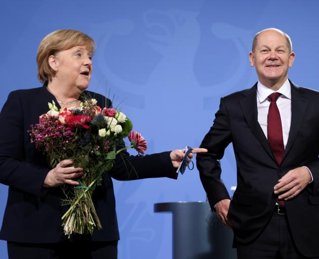 Angela Merkel holds flowers as she hands over the chancellery to her successor, Olaf Scholz, in...